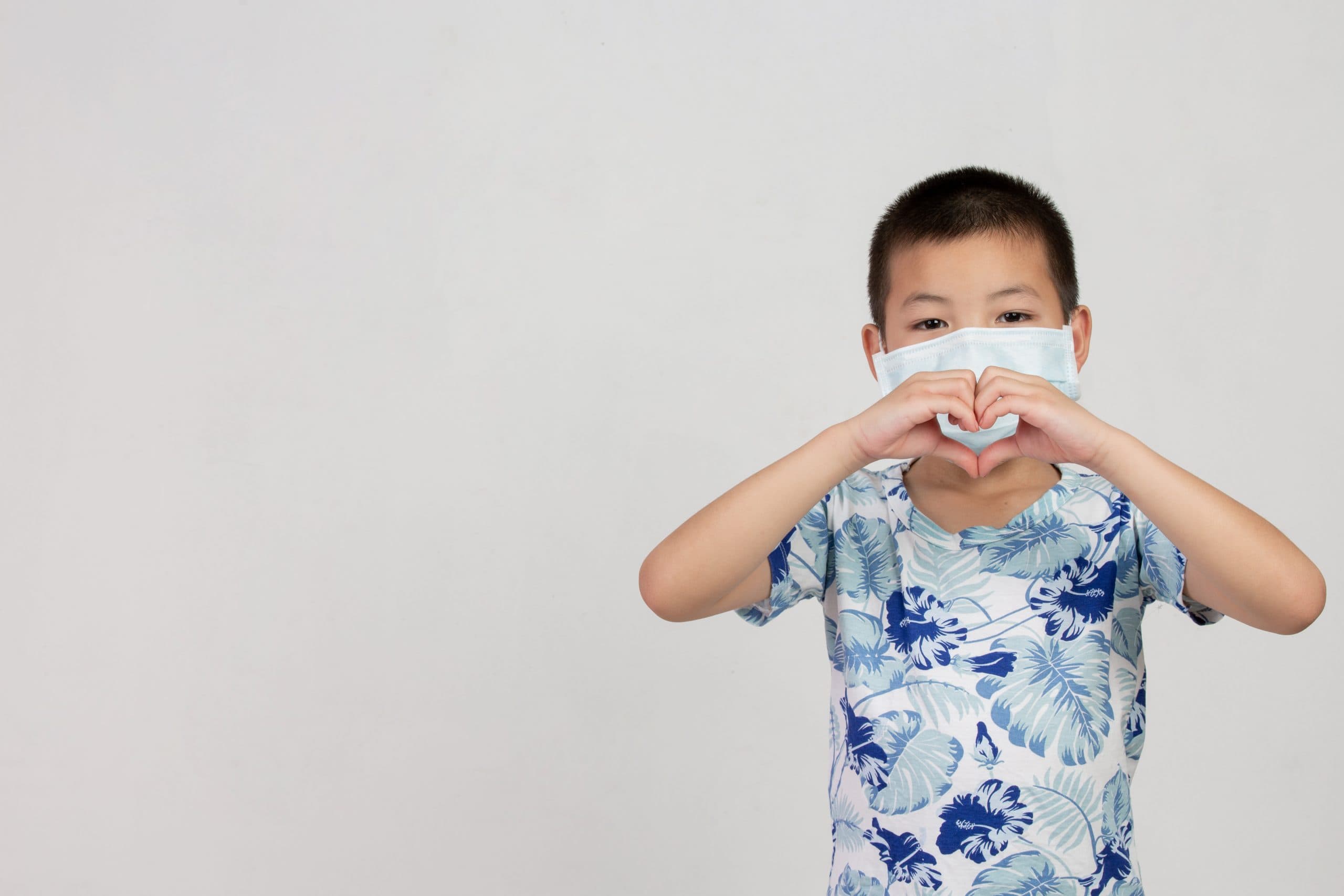 niño usando mascarilla haciendo un corazón con sus manos