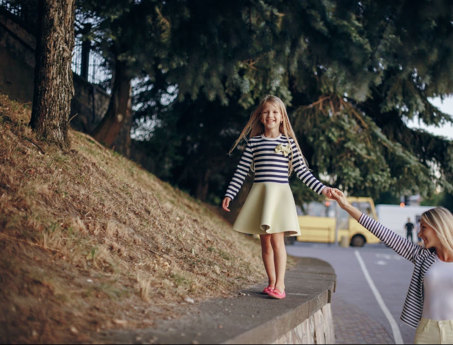 niña caminando en un muro tomada de la mano de su mamá
